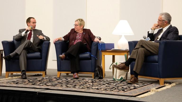 Three speakers sit in leather chairs and talking on the stage at a President's Forum