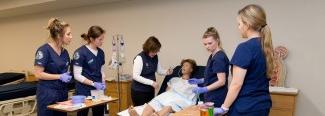 four students and a professor work on a patient simulator