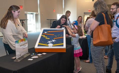 Students instruct a child how tp play with the marble run they built by hand