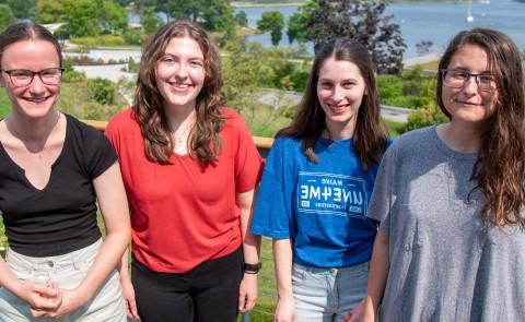 Four students who have received the Millennium Fellowship pose on a campus deck. The campus quad is visible at back